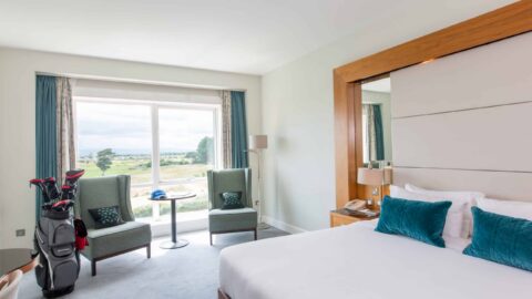 Spacious hotel room with plush bed, seating area, golf course view, and modern decor, inviting a relaxing stay.