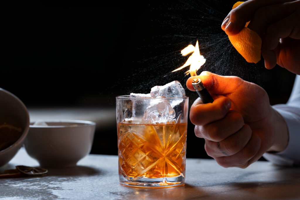Experience a crafted cocktail with flaming orange zest in our elegant hotel bar, offering a warm, inviting atmosphere.