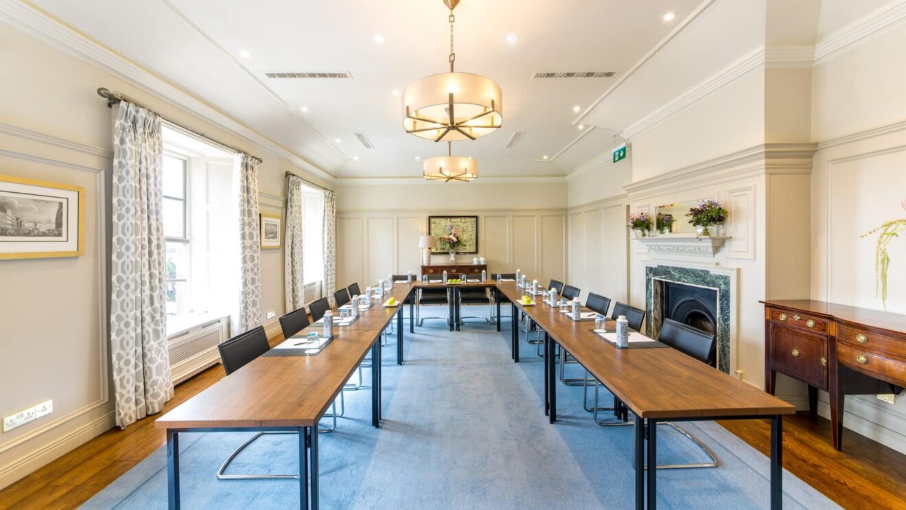 Elegant meeting room with large windows, modern lighting, polished tables, and a fireplace, ideal for business gatherings.