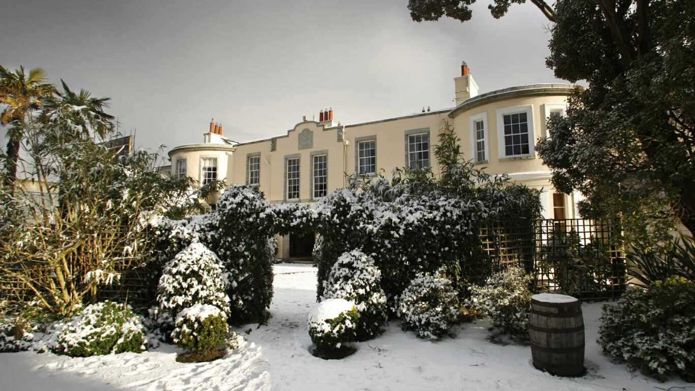 Elegant hotel facade surrounded by snow-covered gardens, offering a cosy winter retreat with charming Georgian architecture.