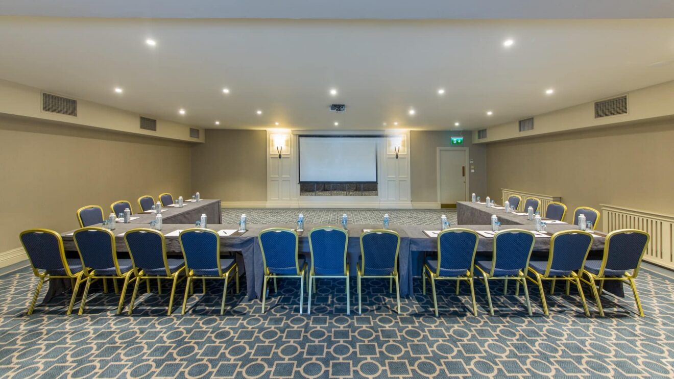 Elegant conference room with modern seating, large screen, bright lighting, and comfortable amenities for meetings.