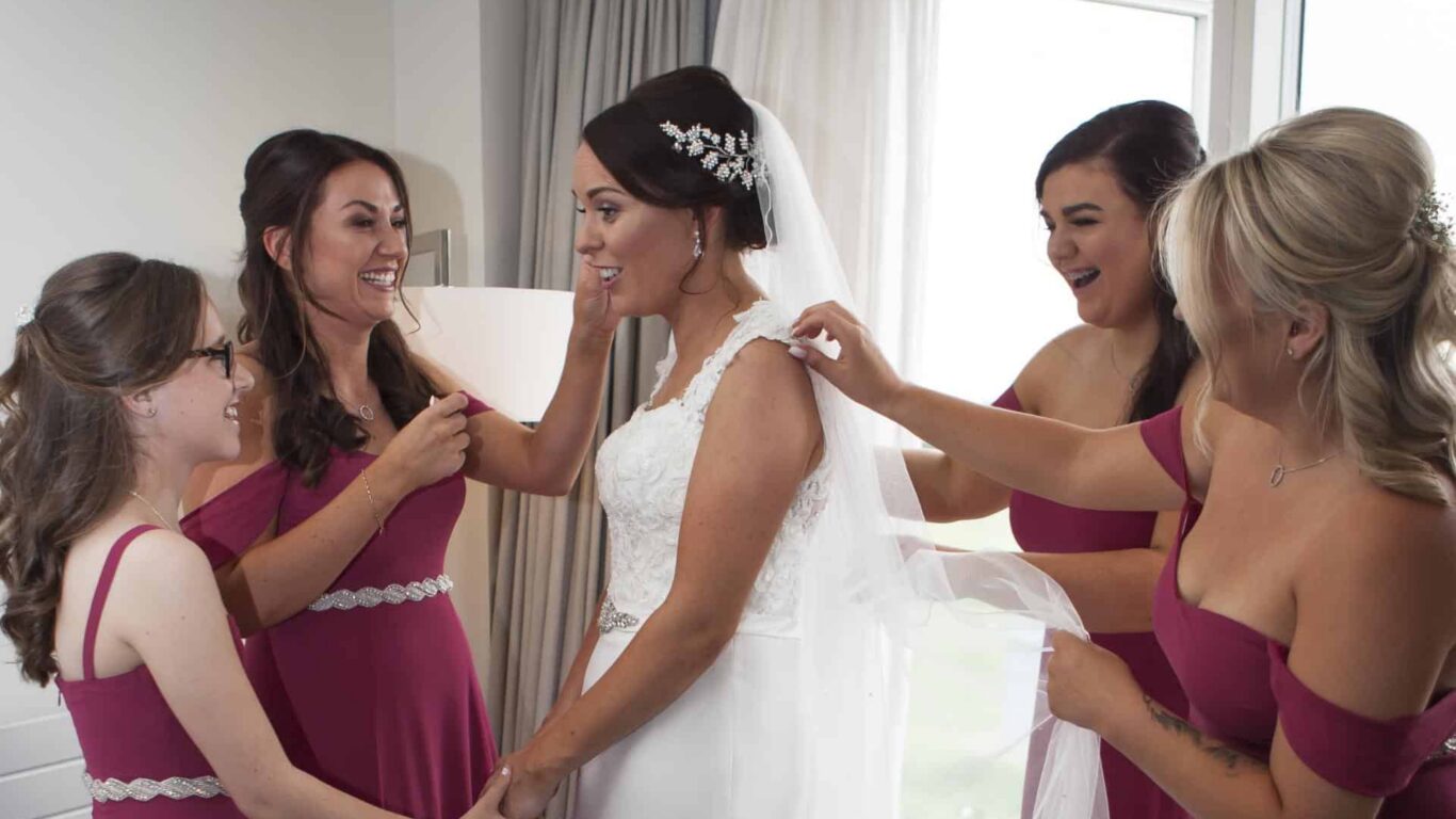Bride and bridesmaids in vibrant dresses enjoy a spacious, elegant hotel room with natural light, perfect for weddings.