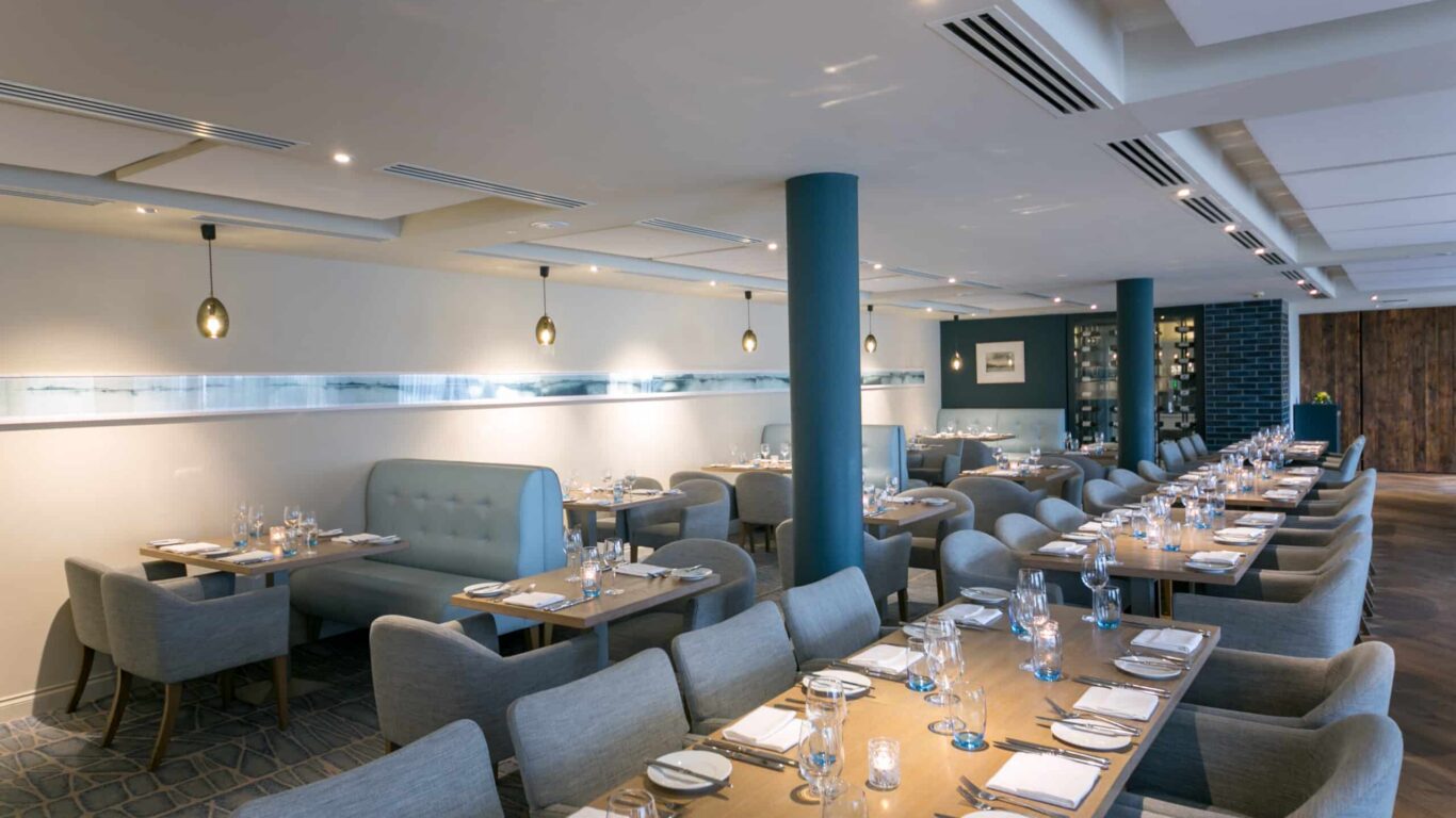 Elegant hotel dining room with cosy grey seating, ambient lighting, set tables, ideal for fine dining experiences.