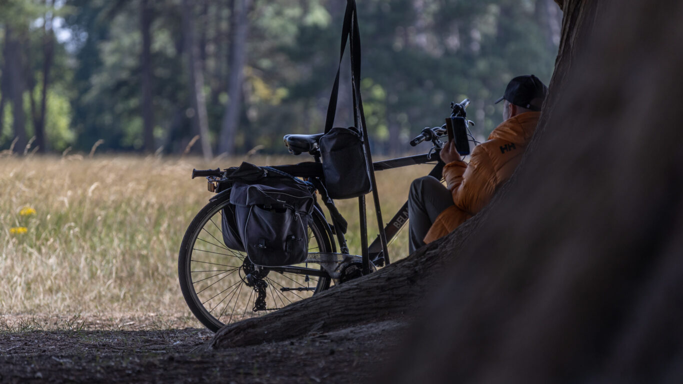 An unrecognizable man sitting in the shade of a tree in Phoenix Park is holding a phone in his hand and a tourist bike is parked in front of him, Phoenix Park, Dublin, Ireland