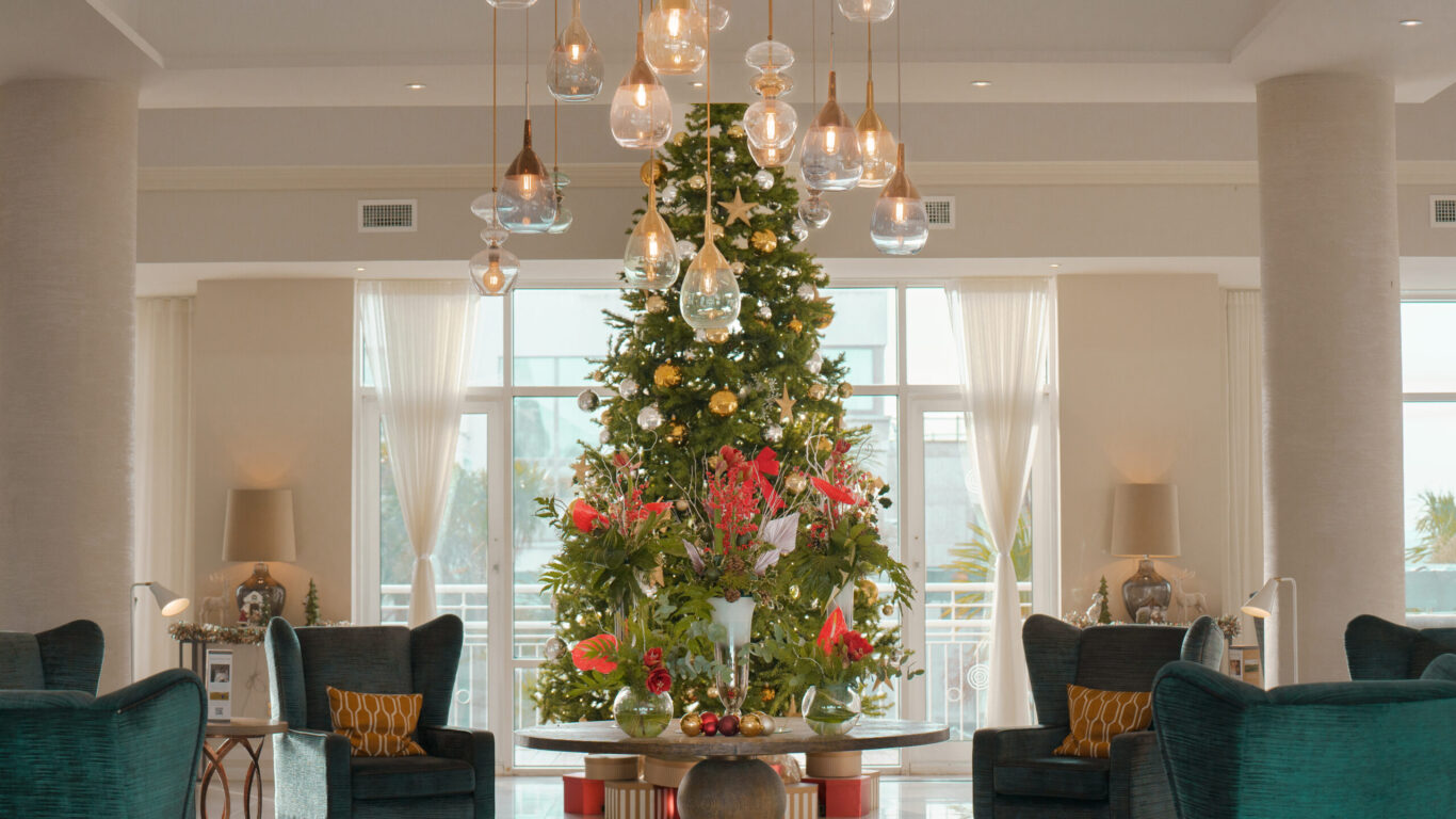 Elegant hotel lobby with festive Christmas tree, chic seating, and modern lighting offering a warm, inviting atmosphere.
