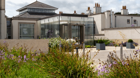 Luxurious hotel entrance with lush gardens and modern glass facade offering a warm welcome to guests seeking comfort and style.