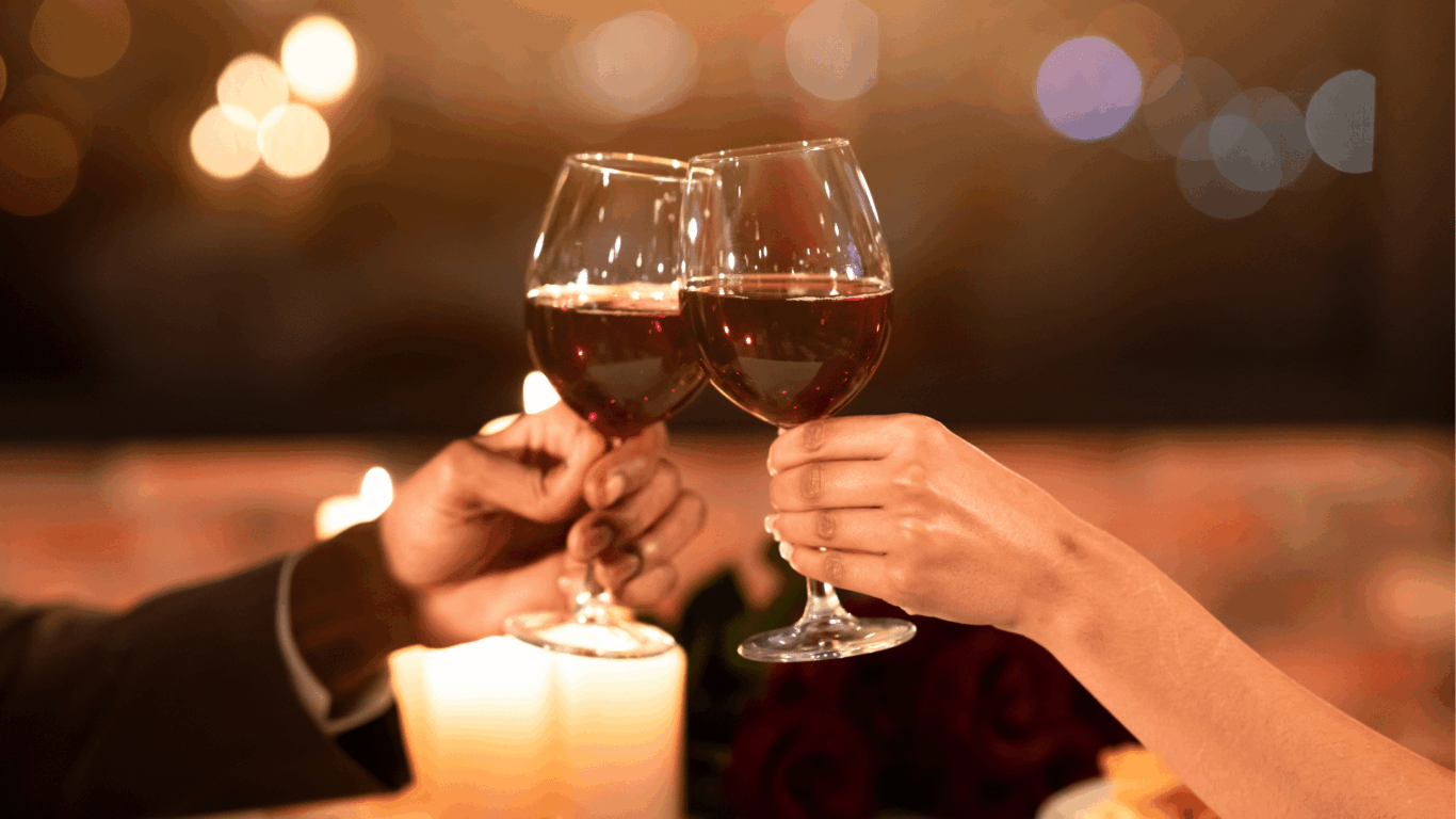 Guests toasting with red wine in a cosy, candlelit setting at the hotel restaurant, suggesting romance and fine dining.