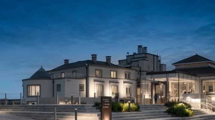 Elegant hotel entrance at dusk with modern glass extension, inviting steps, warm lighting, and lush greenery.