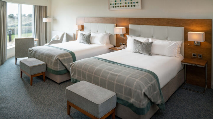 Spacious hotel room with two plush double beds, elegant decor, large window view, and cosy seating area. Ideal for relaxation.