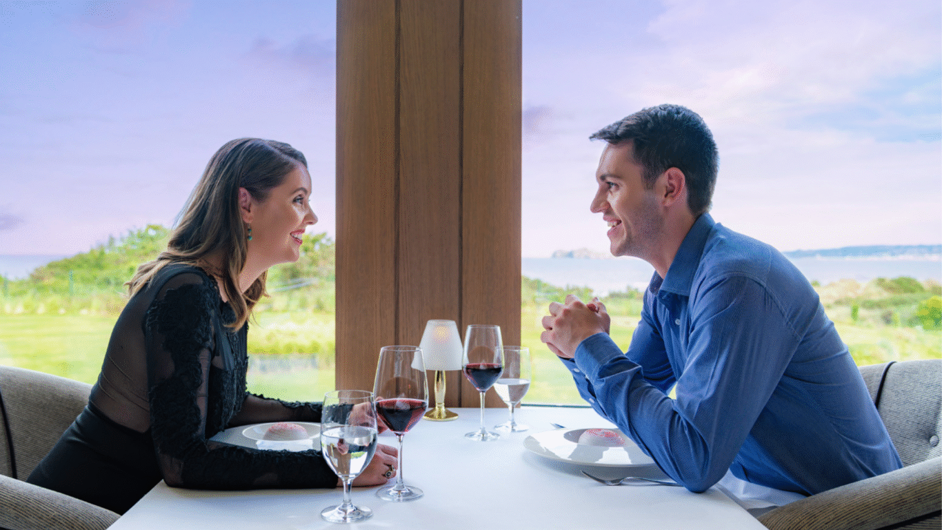 Couple dining with scenic sea-view, enjoying wine at elegant hotel's oceanfront restaurant, offering a romantic ambiance.