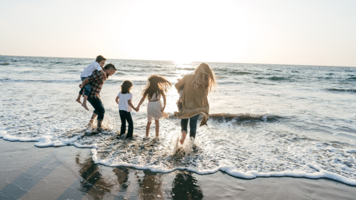 Family enjoying a sunny beach day; kids splash in gentle waves at seaside hotel. Perfect for family-friendly stays.