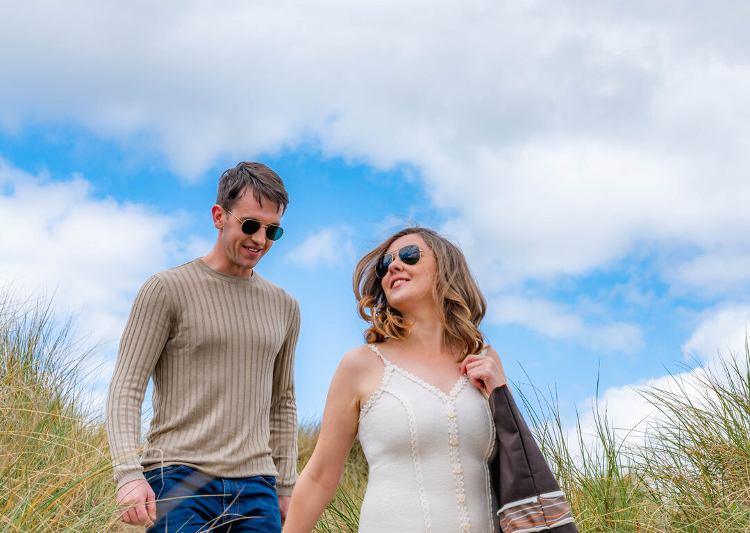 Couple strolling on sandy dunes under a bright blue sky, enjoying a relaxing beach getaway near our hotel.