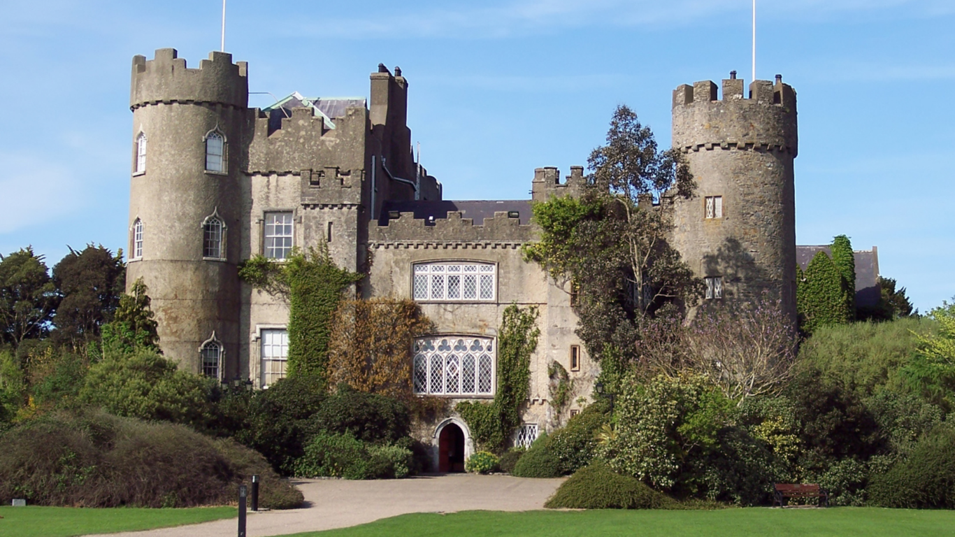 Majestic castle hotel with ivy-covered towers, lush gardens, and historic architecture, offering a serene escape.