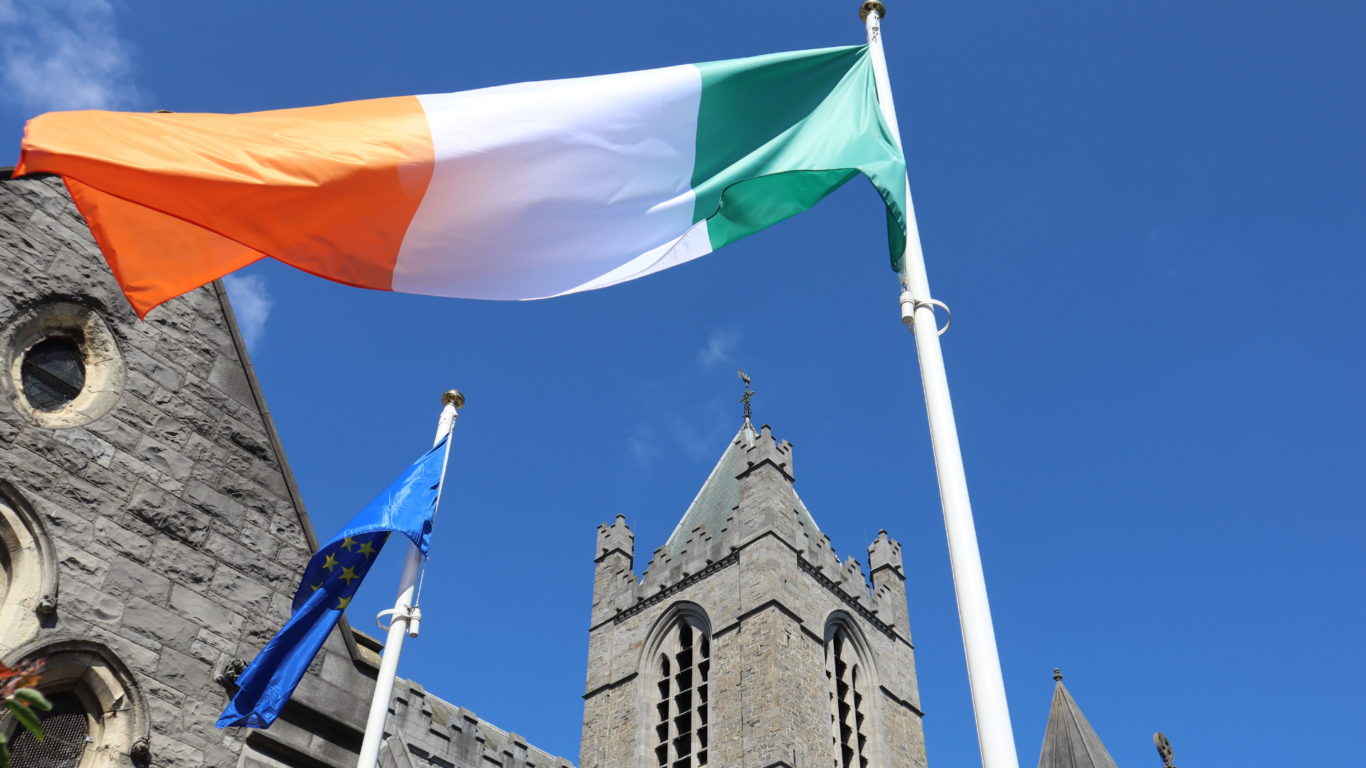 Historic stone church with flying Irish and EU flags against a clear blue sky, offering cultural charm and heritage views.