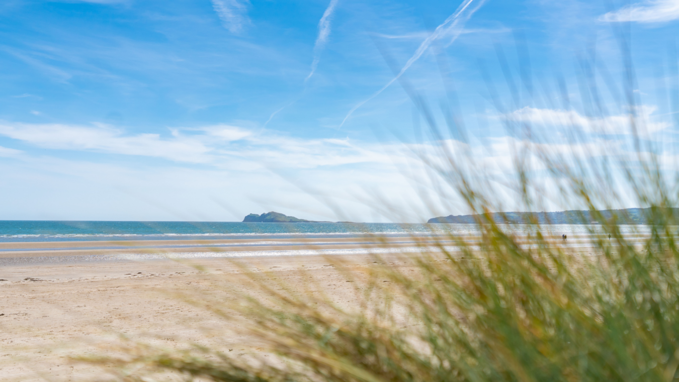Serene sandy beach with clear blue skies, calm sea, and distant cliffs, offering a peaceful seaside escape.
