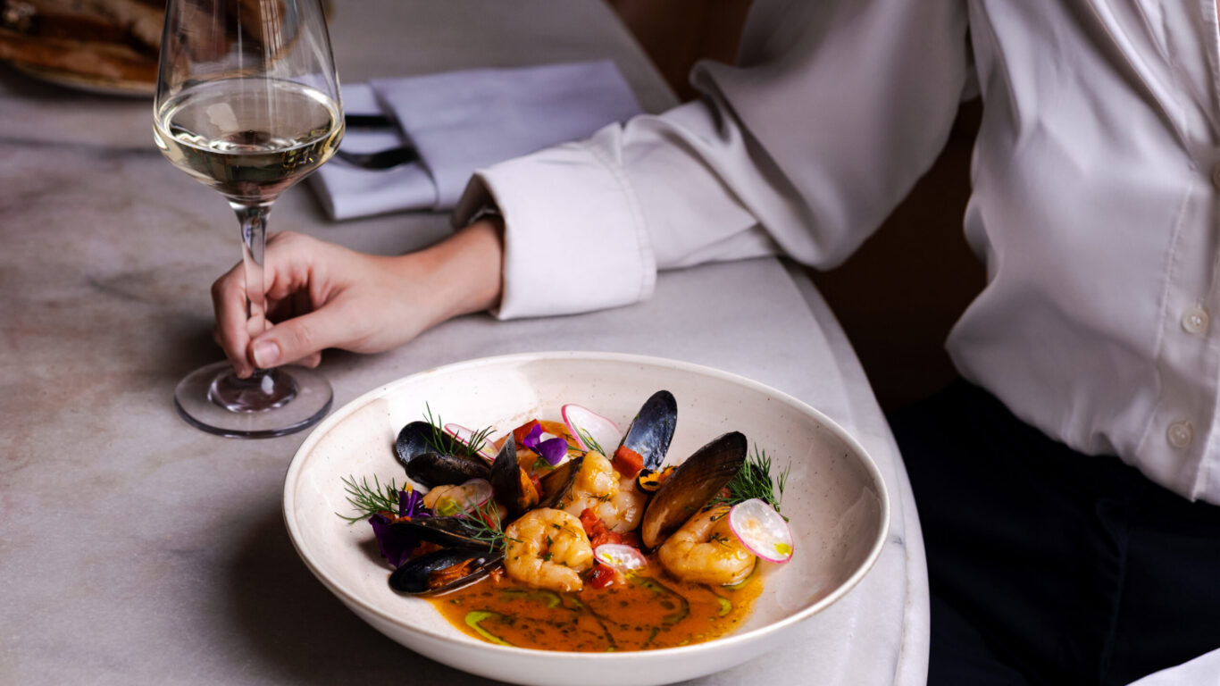Elegant seafood dish with mussels and prawns, complemented by a glass of white wine on a marble table at a luxury hotel restaurant.