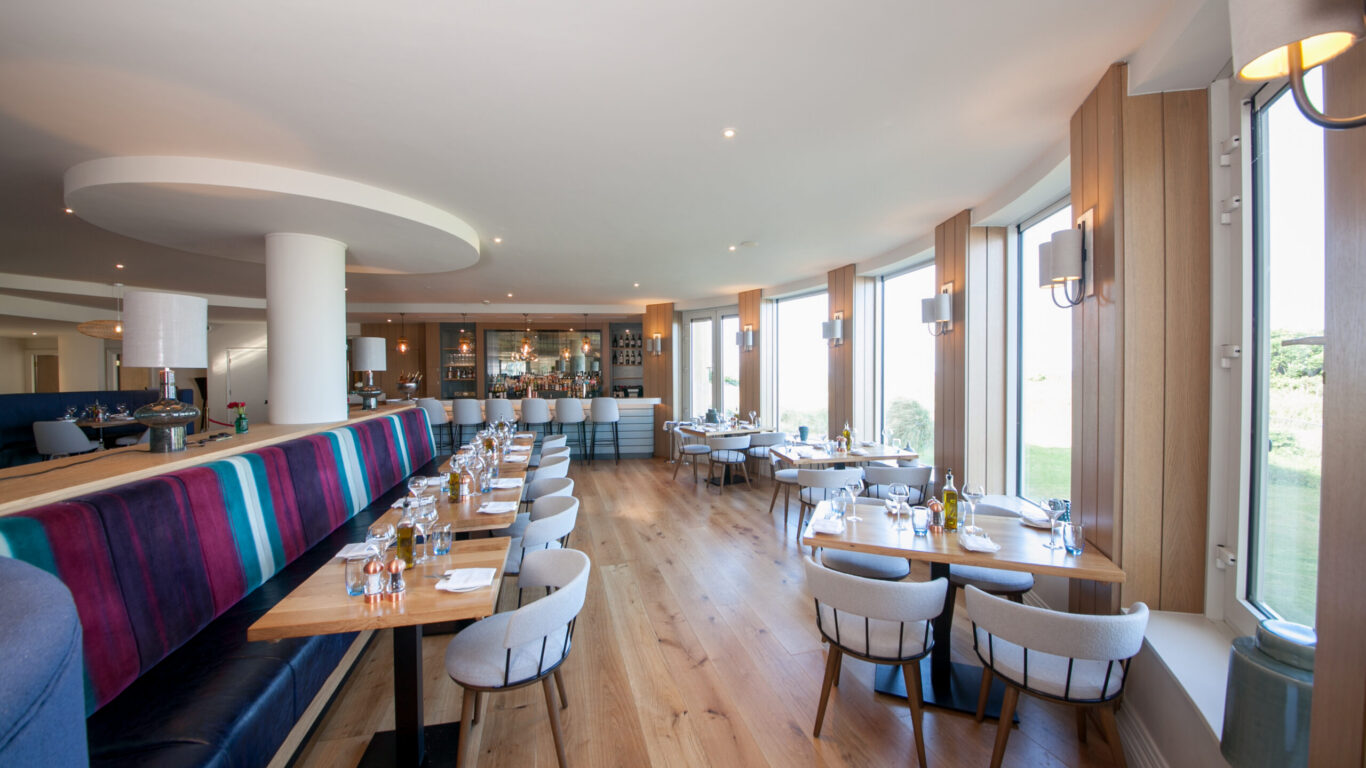 Stylish hotel restaurant with large windows, cosy seating, vibrant d&eacute;cor, and scenic garden views, offering a delightful dining experience.