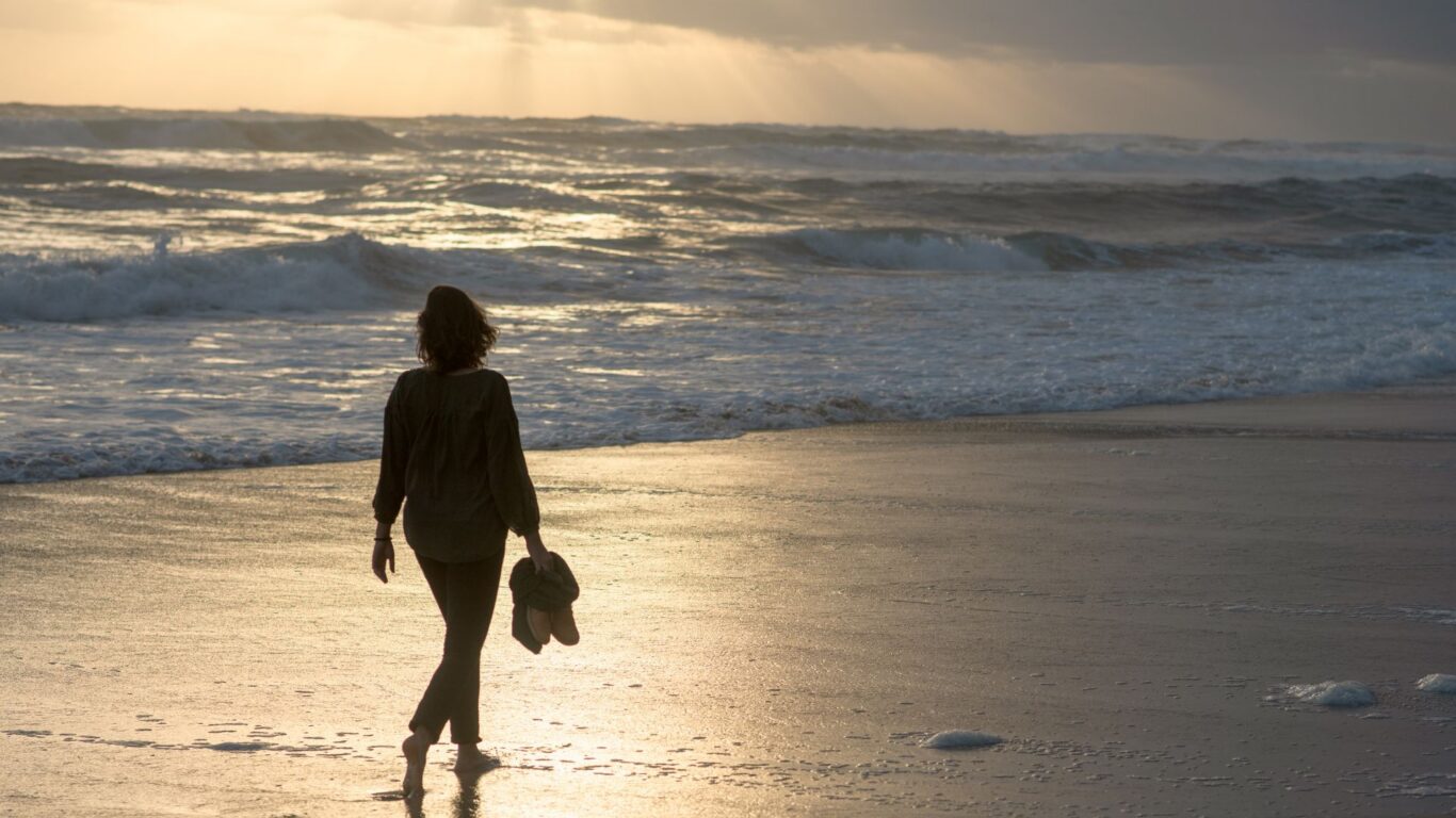 Serene beach walk at sunset; guest enjoys peaceful ocean view, perfect for a calming getaway at our seaside hotel.