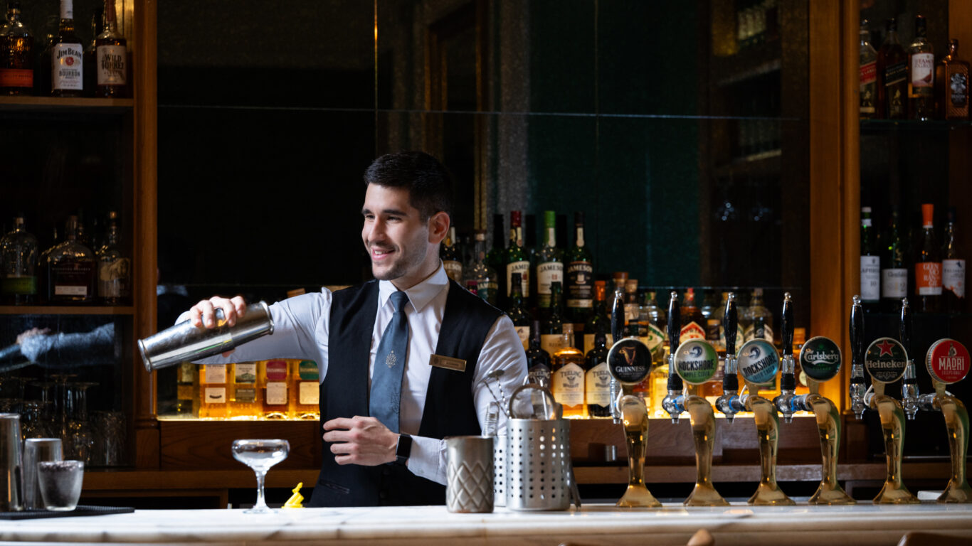 Friendly bartender preparing cocktails at elegant hotel bar with stylish decor and wide drink selection.