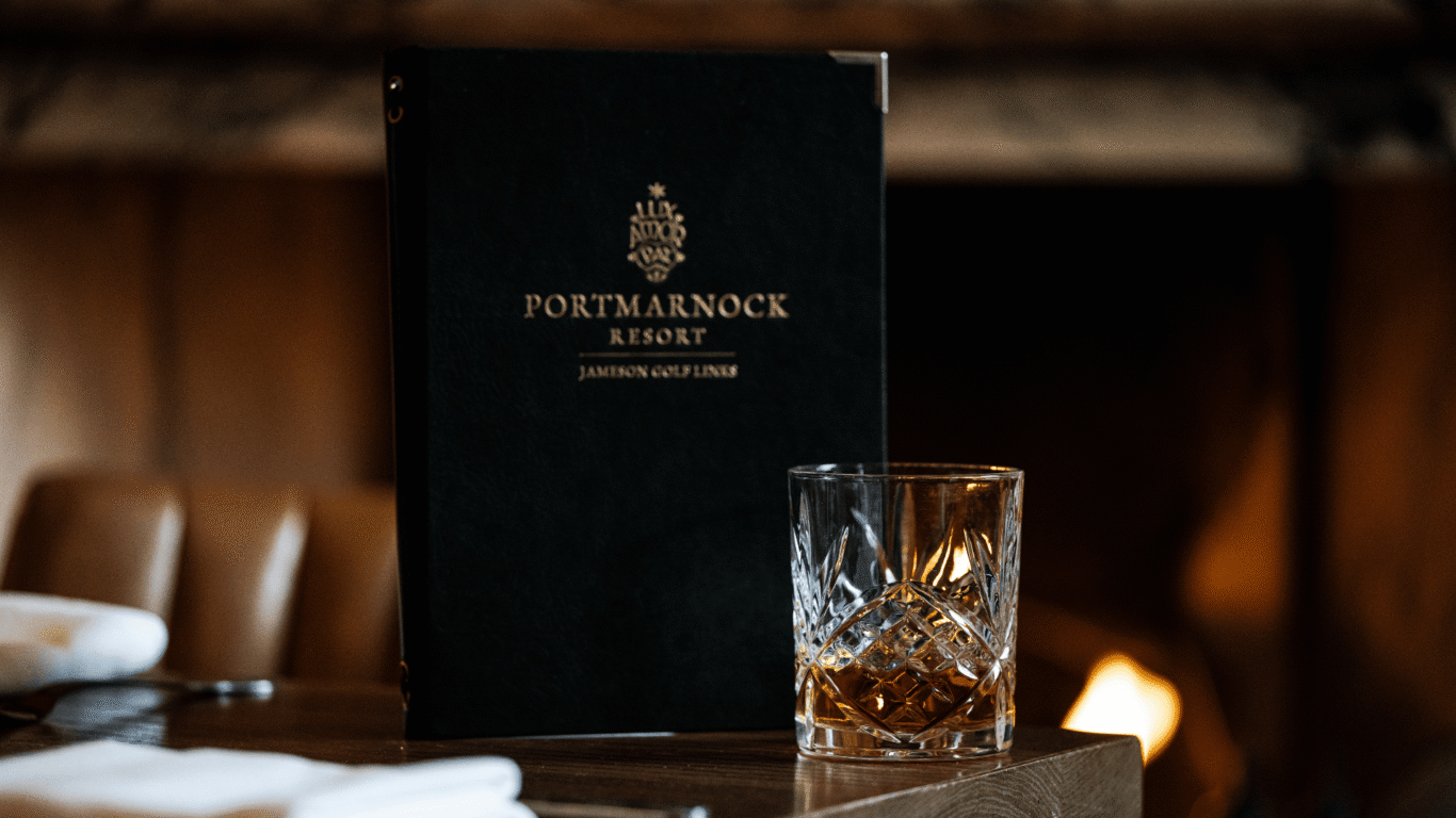 Cosy fireside view at Portmarnock Resort, featuring a luxurious menu and whiskey glass. Perfect for relaxation.