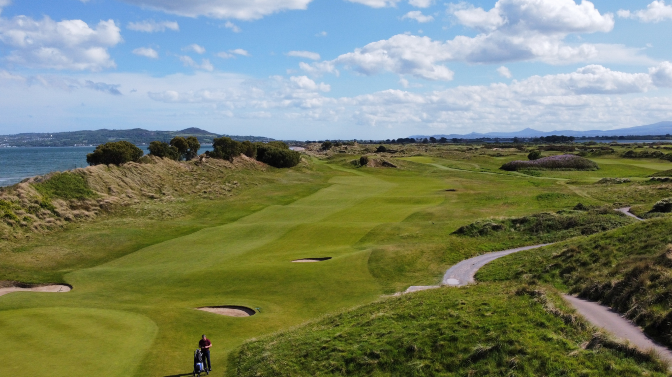 Scenic golf course with lush greens, coastal views, and clear skies, perfect for a relaxing golfing retreat.