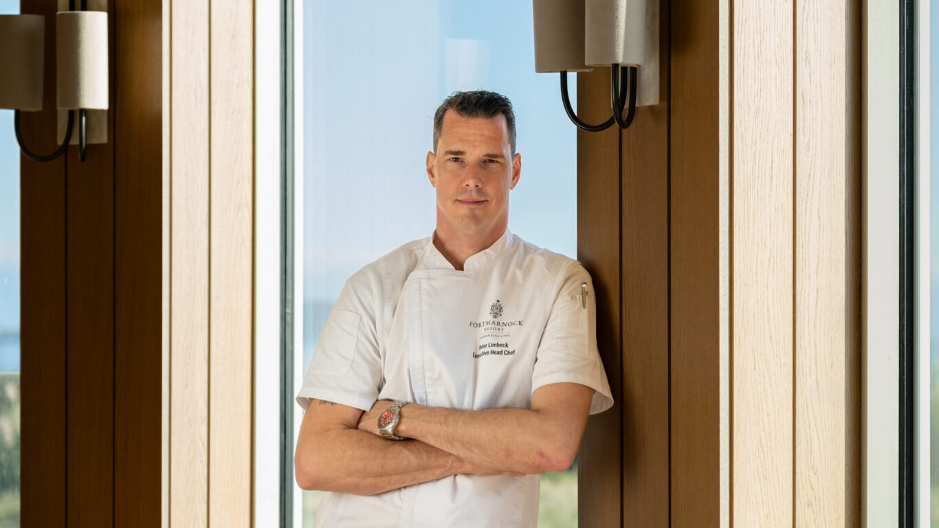 Chef in bright restaurant, standing by large windows offering coastal views, ready to create gourmet experiences.