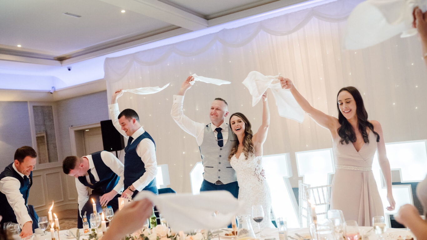 Elegant wedding reception with joyful guests waving napkins, enchanting lighting, luxury event space, creating unforgettable moments.