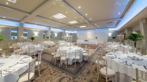 Elegant hotel event ballroom with round tables, white linens, floral centrepieces, and ambient lighting for a perfect celebration.