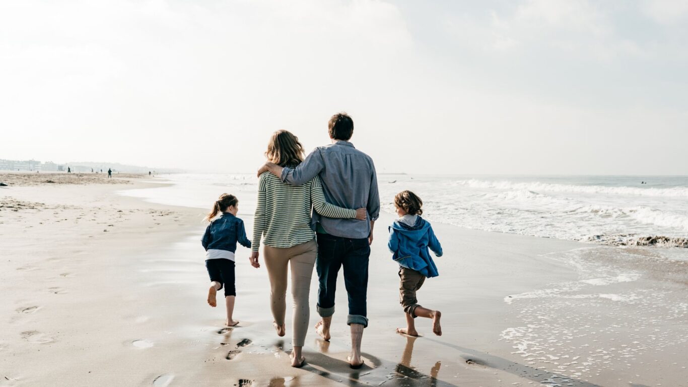 Family walking on a sandy beach near the ocean, enjoying a sunny, relaxing vacation getaway with stunning coastal views.