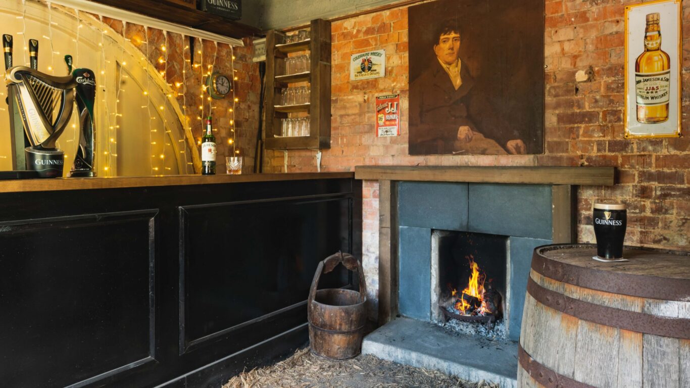 Cosy pub with a crackling fireplace, Guinness on tap, vintage decor, creating a warm, inviting atmosphere for guests.