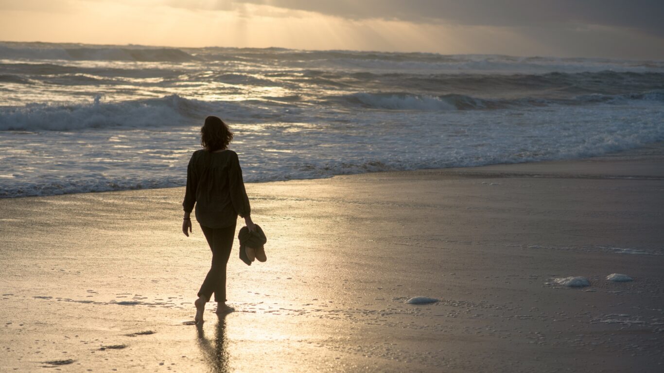 Guest enjoying a serene sunset stroll along the sandy beach near the hotel, with calm waves creating a picturesque view.