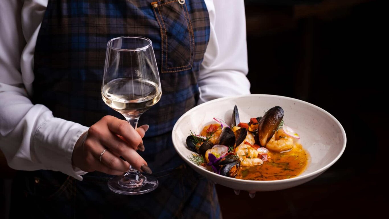 Waiter serving exquisite seafood dish and white wine in elegant restaurant setting at luxury hotel.