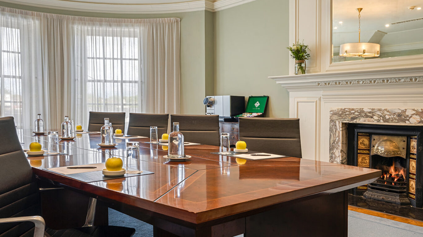 Elegant meeting room with wooden table, plush chairs, decorative lighting, and a cosy fireplace, perfect for business events.
