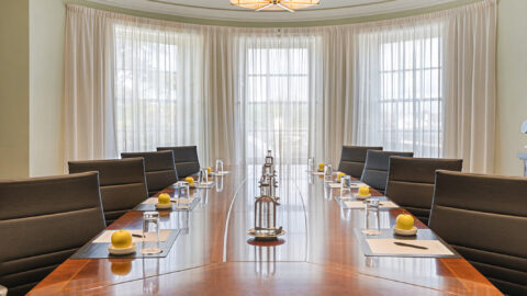 Elegant boardroom with a polished table, plush chairs, chic chandeliers, ideal for productive meetings at luxury hotel.