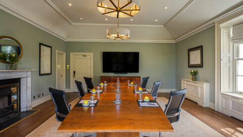 Elegant meeting room with large wooden table, comfy chairs, smart TV, natural light, ideal for conferences or business events.