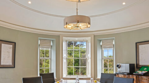 Elegant boardroom with wooden table, comfy chairs, and window views, perfect for meetings; water bottles, pads, apples.