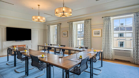 Elegant meeting room with natural light, large windows, modern decor, conference tables, and a large TV screen.