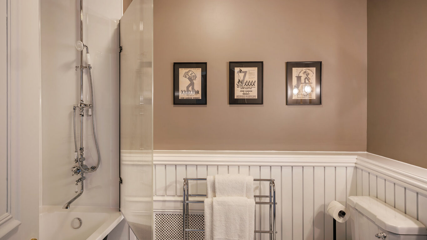 Elegant hotel bathroom with classic bath, vintage taps, framed art, and plush towels on a heated rack.