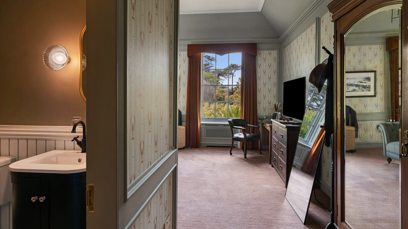 Elegant hotel room with vintage decor, comfy chairs, large mirror, and lush garden view from window. Luxurious and cosy stay.