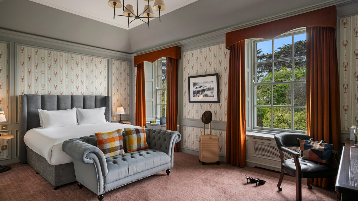 Elegant hotel room with plush bed, stylish armchair, and large window overlooking lush garden; cosy and inviting.