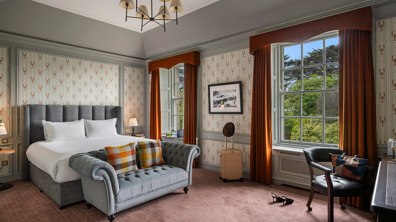 Elegant hotel room with plush bed, stylish armchair, and large window overlooking lush garden; cosy and inviting.