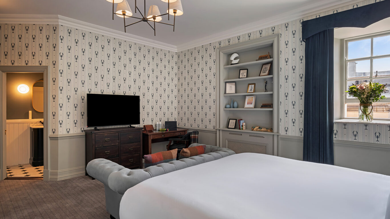 Elegant hotel room with king bed, stylish decor, large TV, cosy seating, desk, and window views.