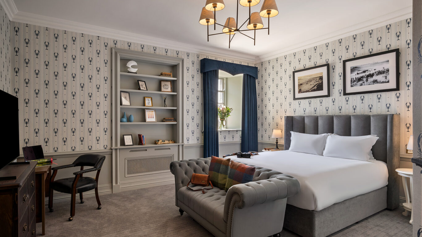 Elegant hotel room with king-size bed, cosy sofa, classic decor, desk, and window view. Enjoy a relaxing stay.