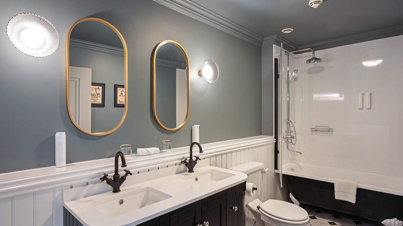 Elegant hotel bathroom with double sinks, gold mirrors, shower bath, and ambient lighting, offering a relaxing retreat.