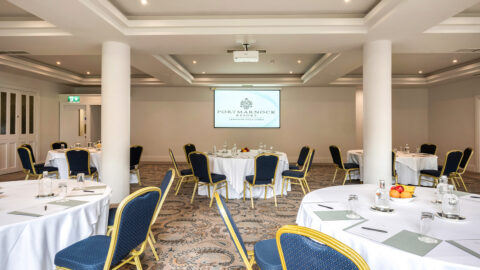 Elegant hotel conference room with round tables, blue chairs, and stylish decor, perfect for meetings or events.