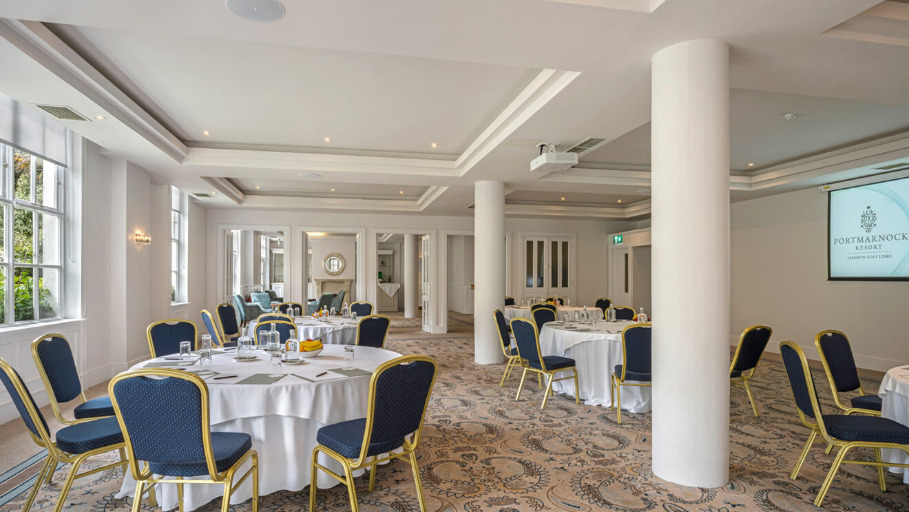 Elegant, spacious hotel conference room with round tables, blue chairs, chic decor, natural lighting, ideal for events.