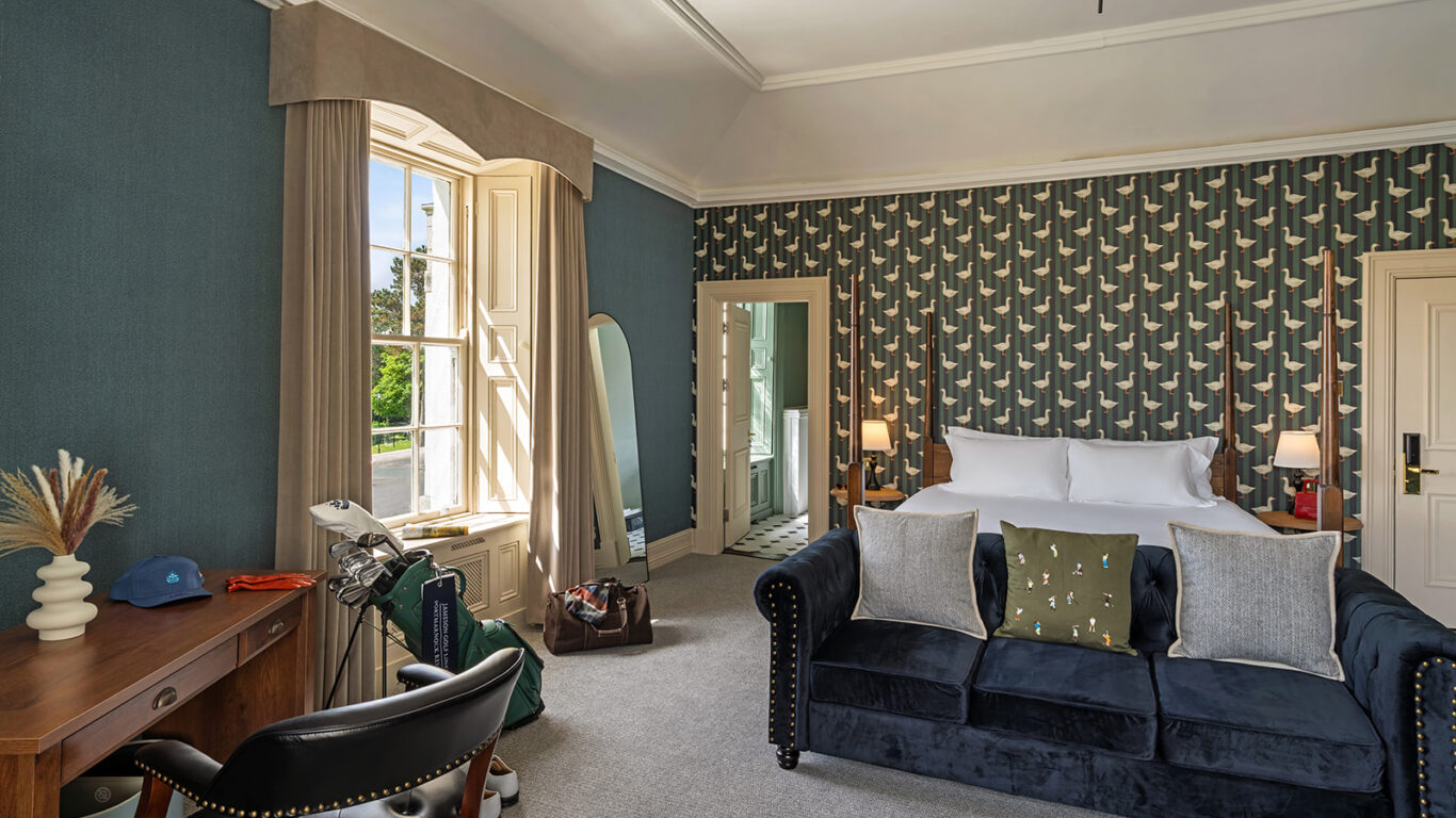 Elegant hotel room with plush velvet sofa, king-size bed, stylish wallpaper, and large window with garden view. Luxurious stay.