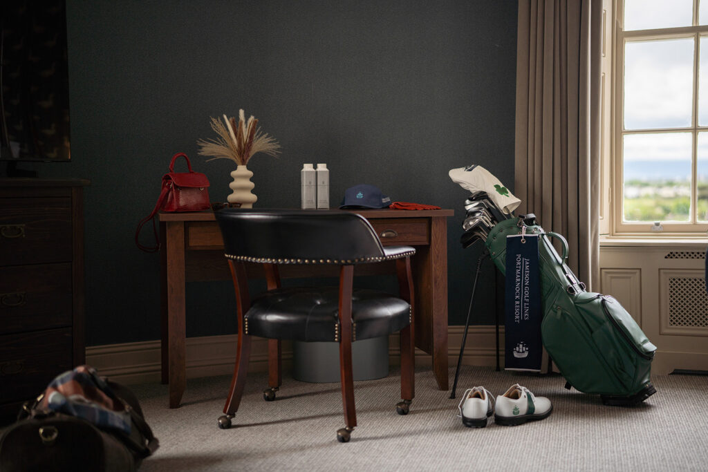 Golf-Friendly Hotel Room Cosy hotel room with golf gear, comfy chair, elegant desk, natural light from window, ideal for golf enthusiasts.