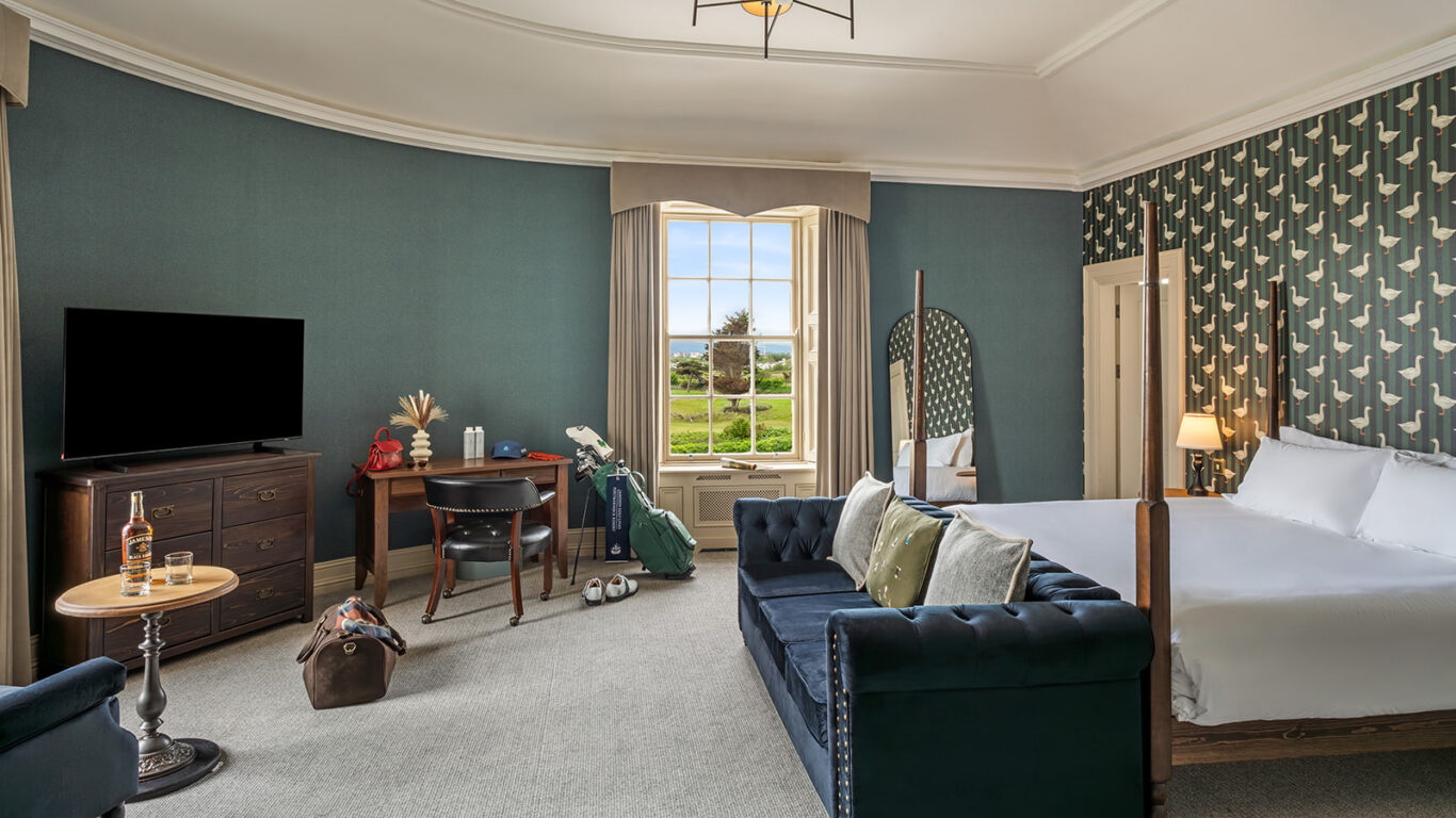 Elegant hotel room with a plush bed, stylish decor, cosy seating, and a window view of lush gardens. Relax and unwind.