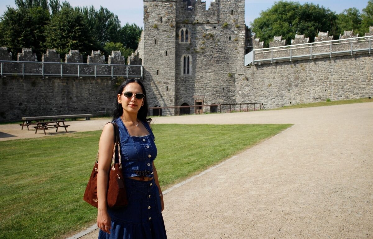 Woman enjoys sunny day at historic castle grounds with lush greenery.